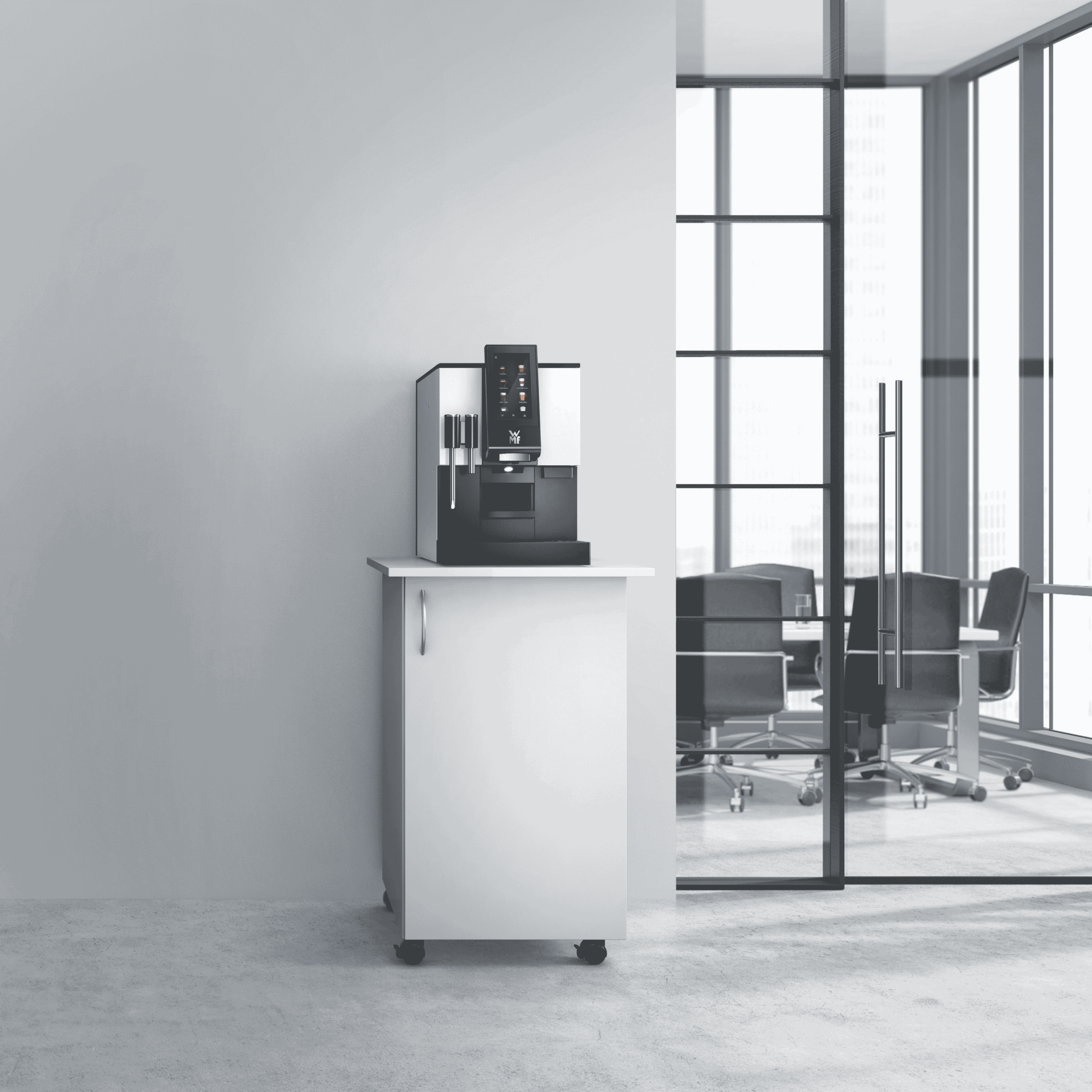 Nowoczesny ekspres do kawy WMF 1100 S stoi na białej szafce na kółkach, ustawionej przy ścianie w biurowym wnętrzu. W tle widoczne są przeszklone drzwi i sala konferencyjna z czarnymi krzesłami i dużymi oknami wpuszczającymi naturalne światło.