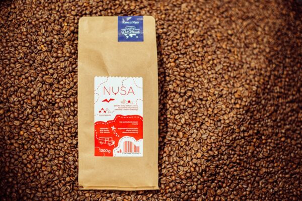 Kilogramowe opakowanie kawy Nysa CaffeDelMondo na tle palonej kawy.