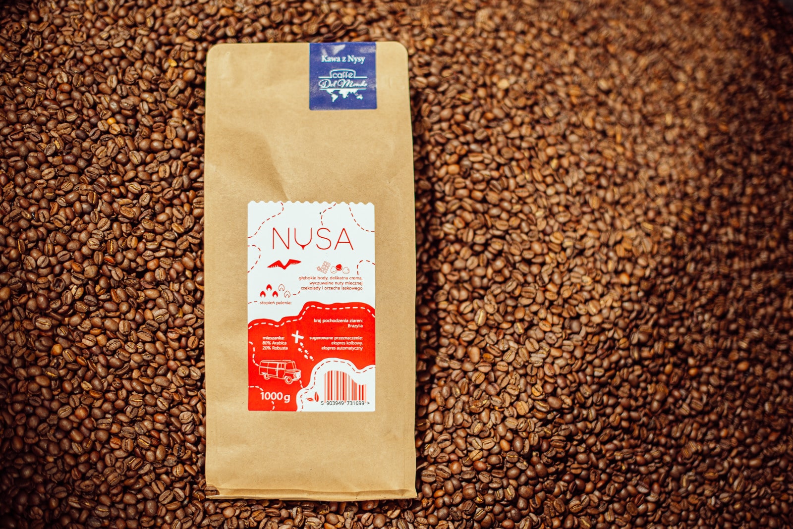 Kilogramowe opakowanie kawy Nysa CaffeDelMondo na tle palonej kawy.